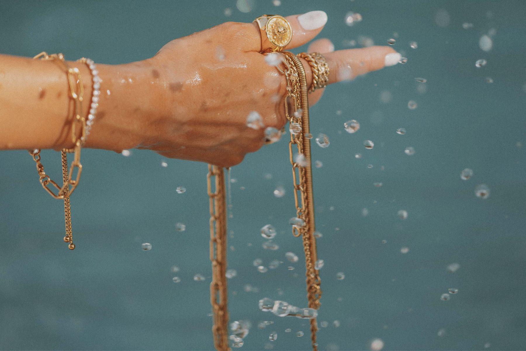 Hand holding gold jewelry out of water with drops